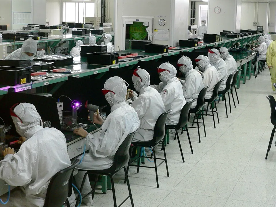 Pekerja berpakaian cleanroom merakit komponen di lini produksi pabrik elektronik di Shenzhen